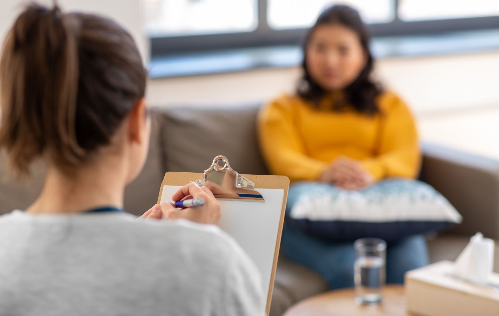 A woman is sitting on a couch talking to a female psychologist.