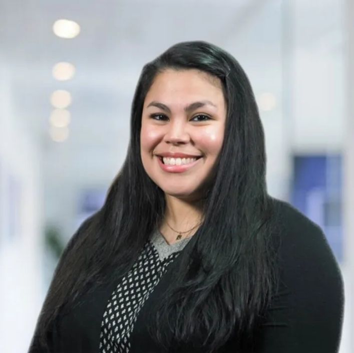 A woman with long black hair is smiling for the camera in a hallway.