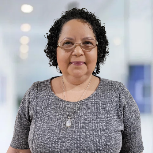 A woman wearing glasses and a necklace is standing in a hallway.
