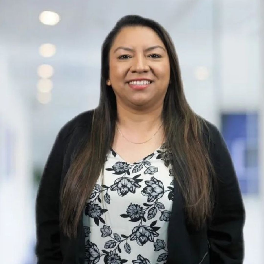 A woman wearing a black jacket and a floral shirt is smiling for the camera.