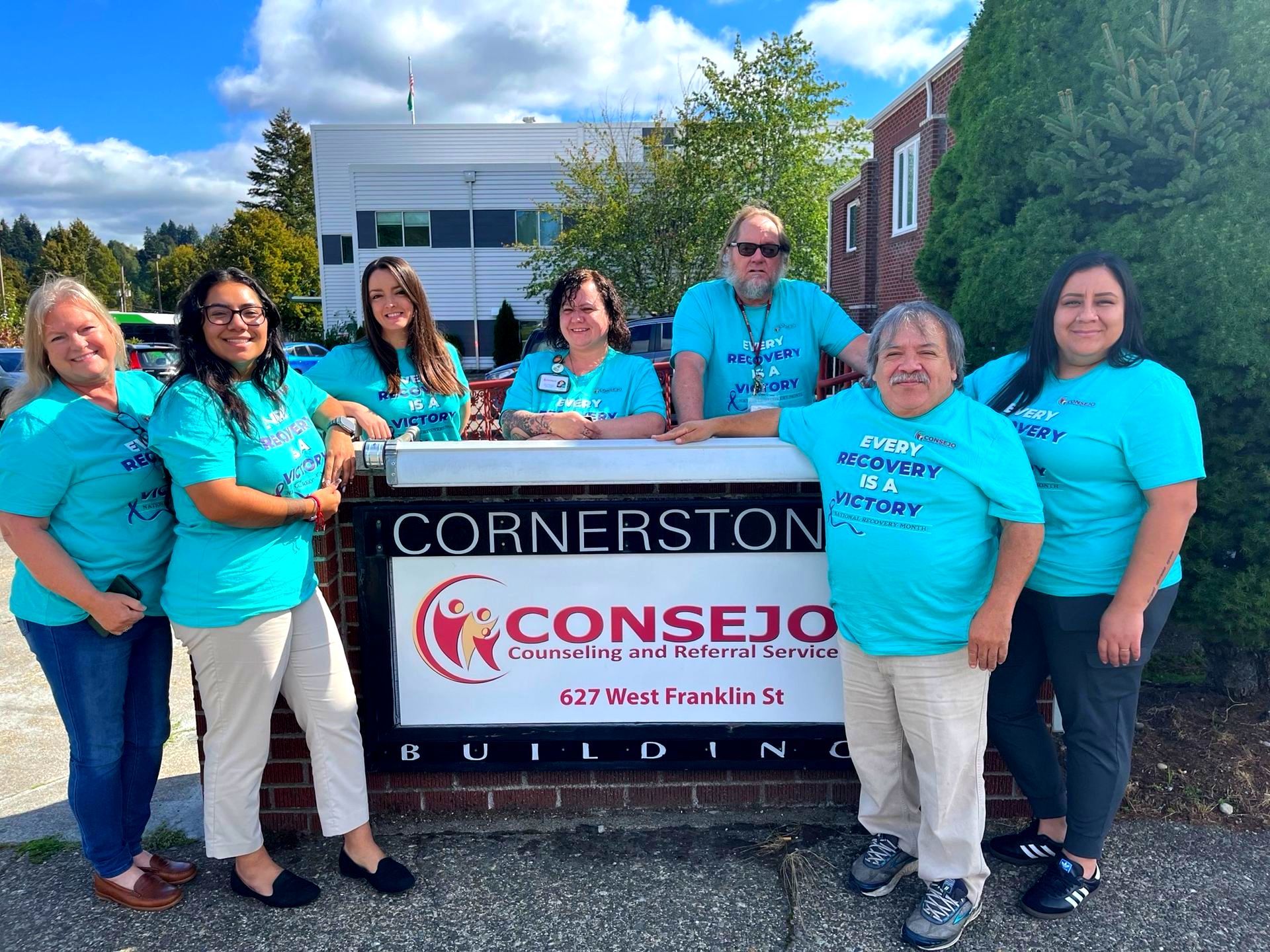 A group of people are posing for a picture in front of a cornerston building.