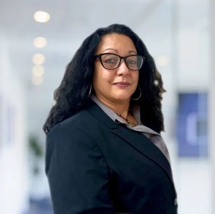 A woman wearing glasses and a suit is standing in a hallway.