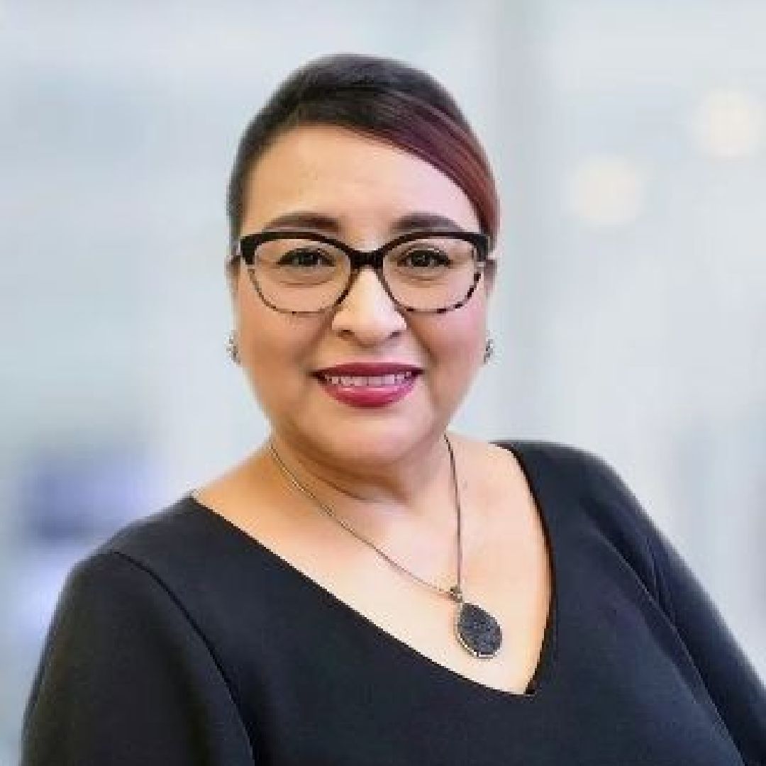 A woman wearing glasses and a necklace is smiling for the camera.