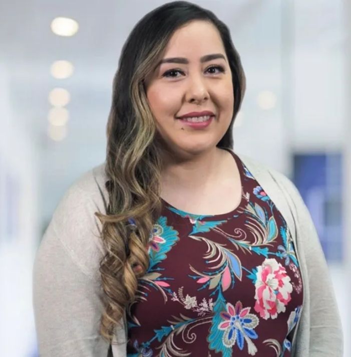 A woman wearing a floral shirt and a cardigan is smiling for the camera.