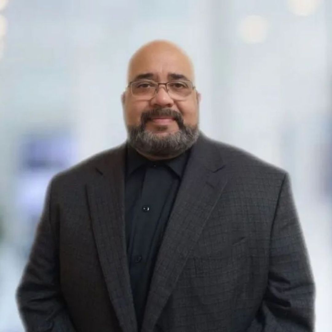 A man with a beard and glasses is wearing a suit and black shirt.