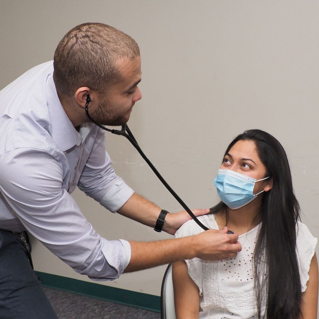 A man is using a stethoscope on a woman wearing a mask