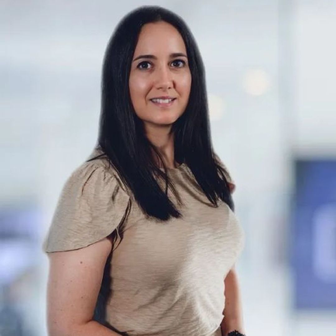 A woman in a tan shirt is smiling for the camera.