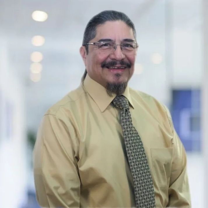 A man wearing glasses and a tie smiles for the camera