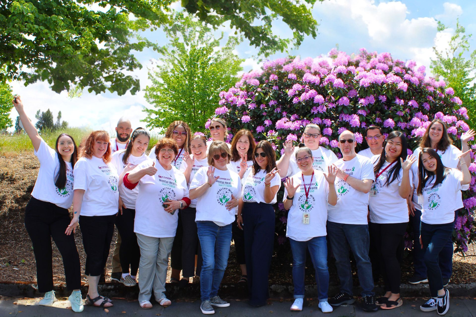 A group of people are posing for a picture in front of a bush with purple flowers.