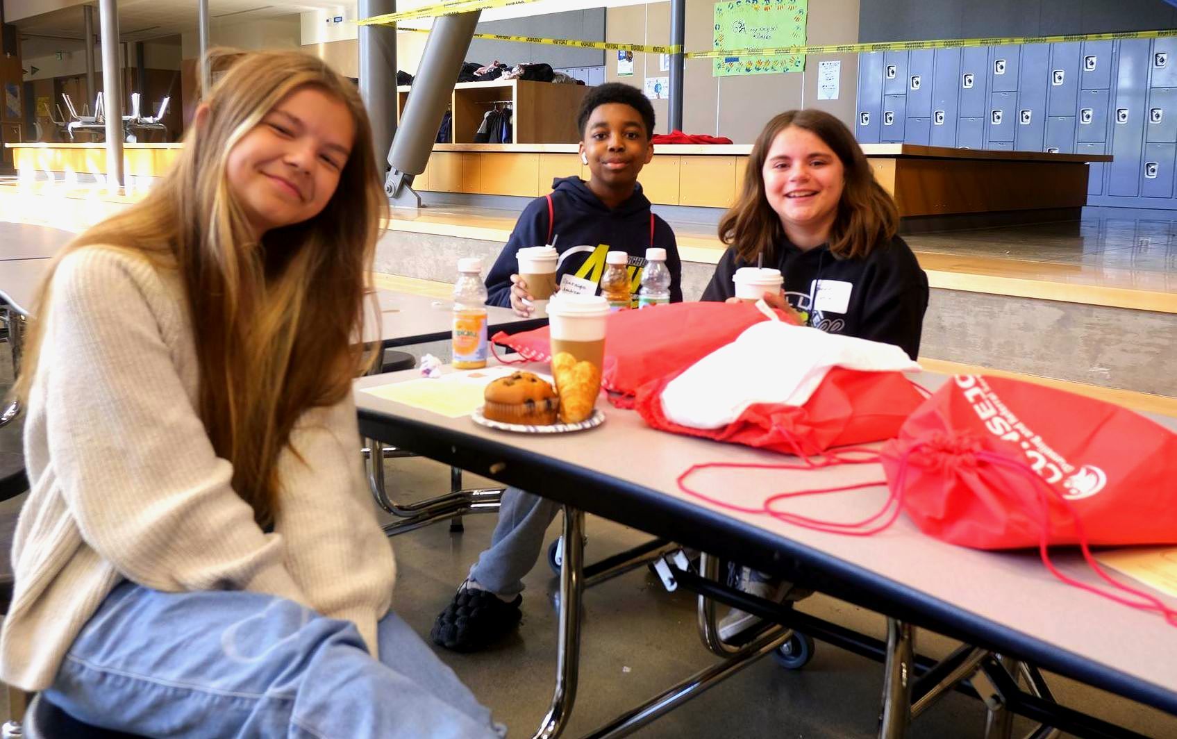 A group of young people are sitting at a table in a school cafeteria.