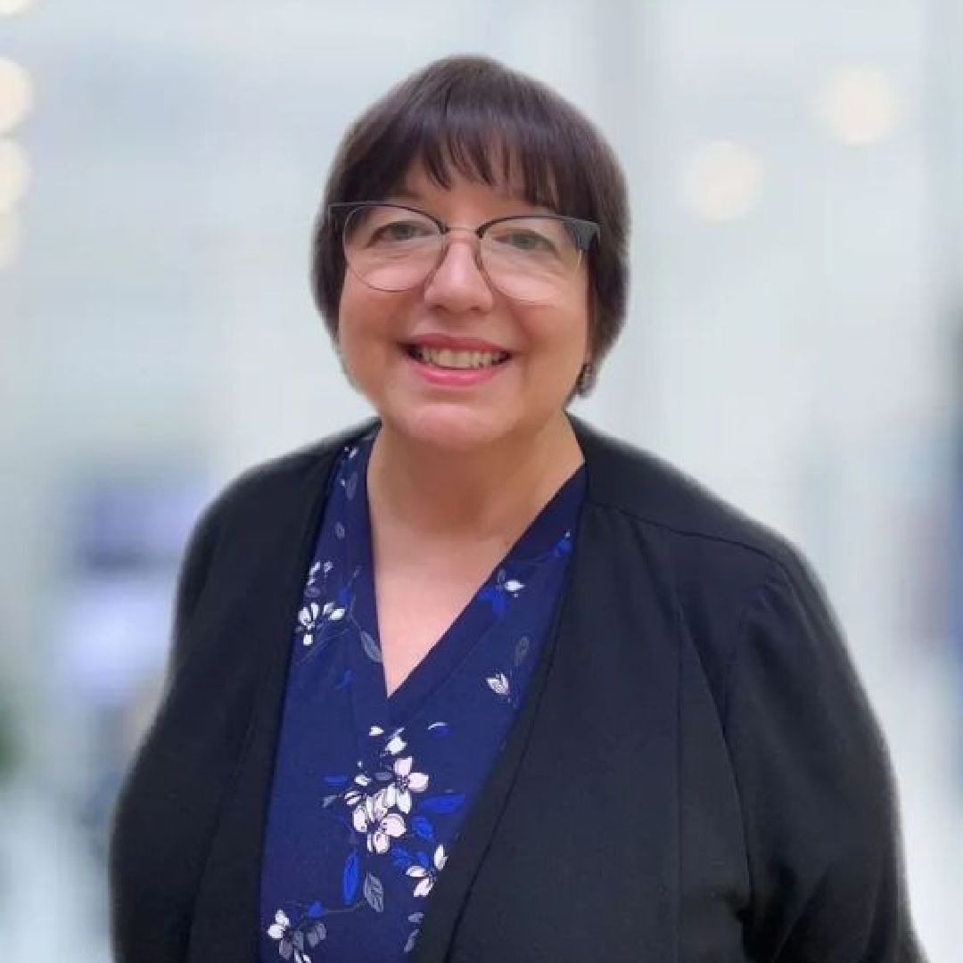 A woman wearing glasses and a black jacket is smiling for the camera.