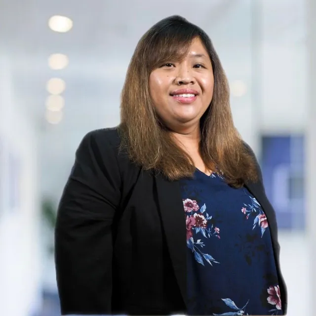 A woman wearing a black jacket and a blue floral shirt is smiling for the camera.