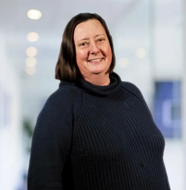 A woman in a blue sweater is smiling for the camera.