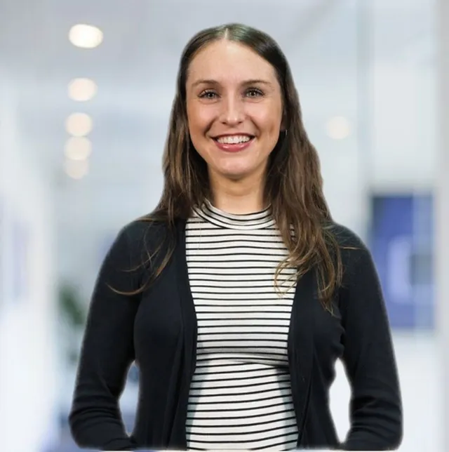 A woman wearing a striped shirt and a black cardigan smiles for the camera