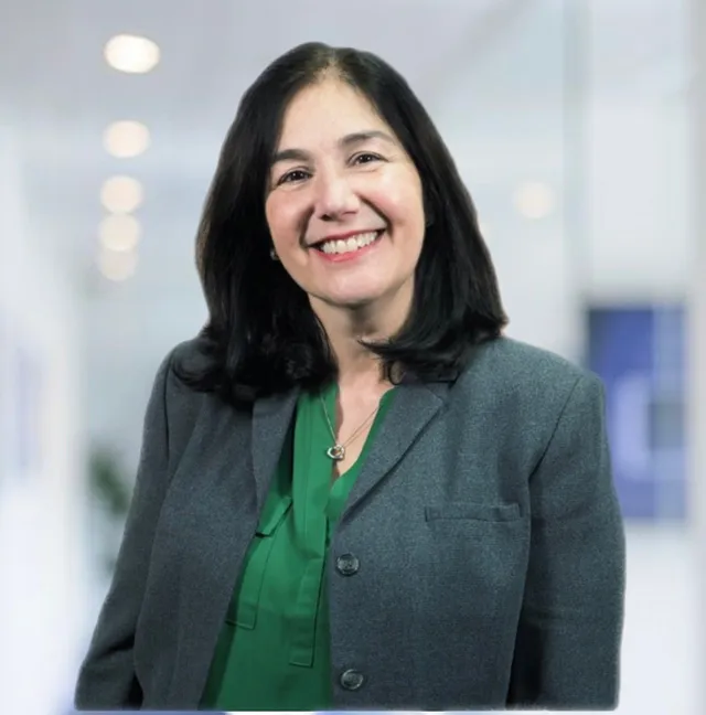 A woman wearing a grey jacket and a green shirt smiles for the camera