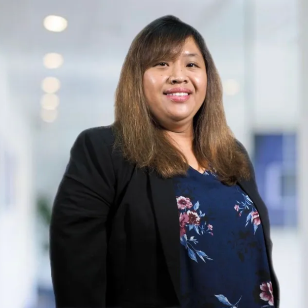 A woman wearing a black jacket and a blue floral shirt is smiling for the camera.