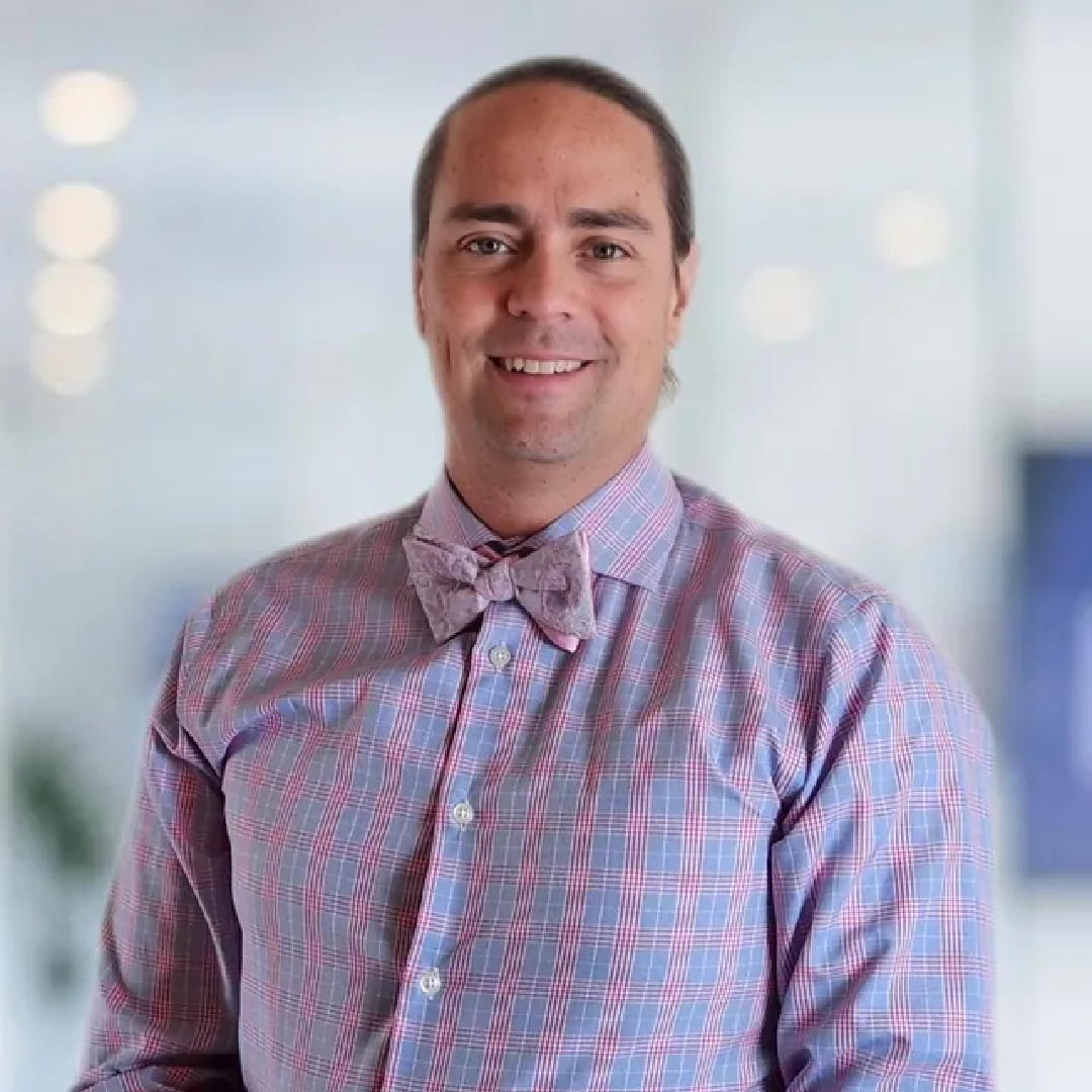 A man in a plaid shirt and bow tie is smiling for the camera.