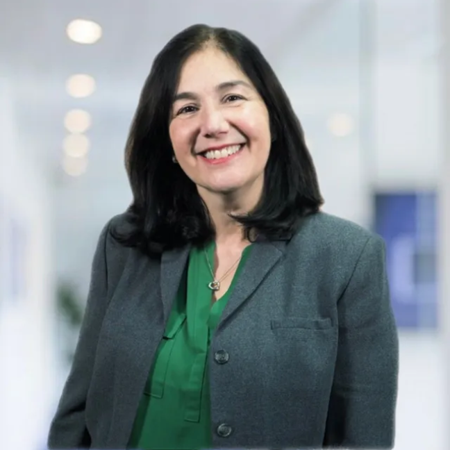 A woman wearing a grey jacket and a green shirt smiles for the camera