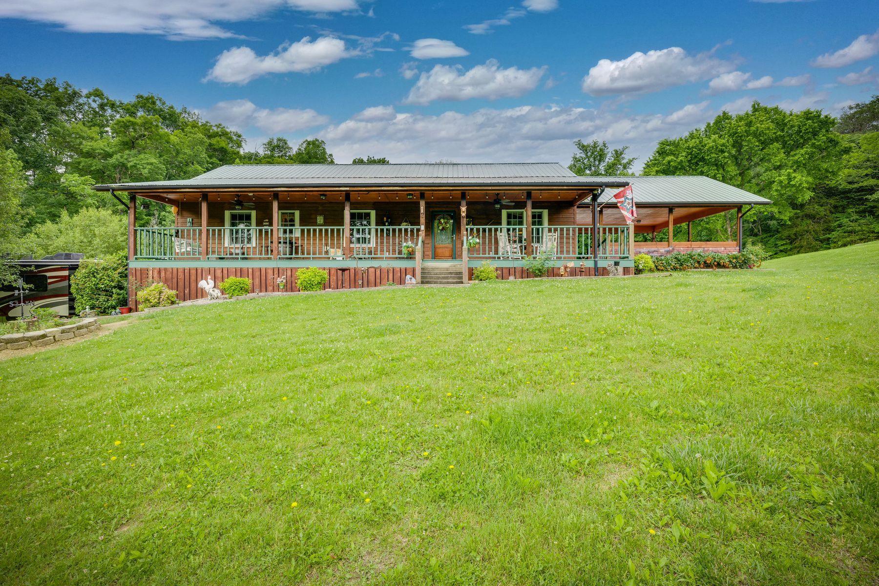 Large house with a large porch is sitting on top of a lush green hill.