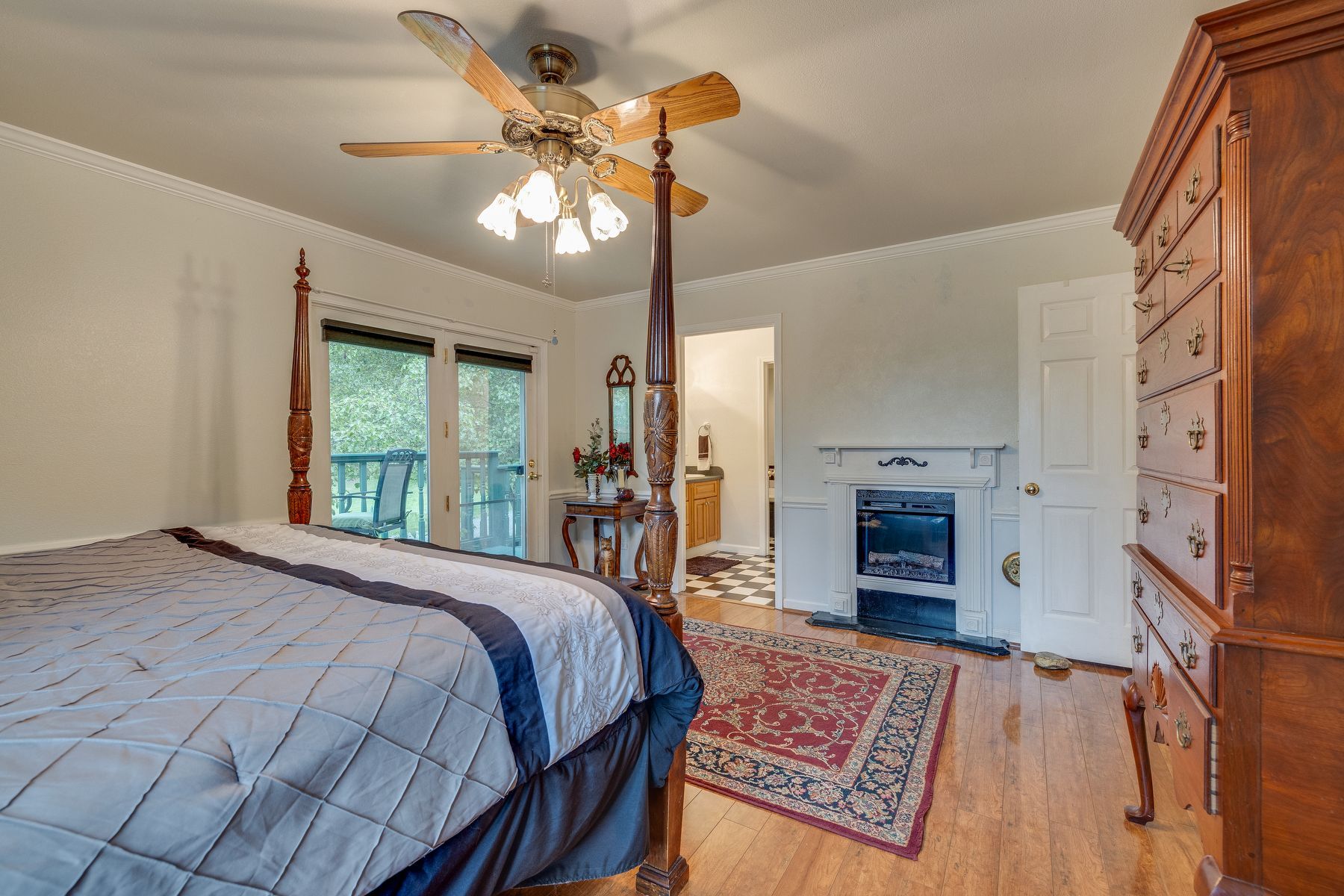 Bedroom with a four poster bed , ceiling fan , dresser and fireplace.