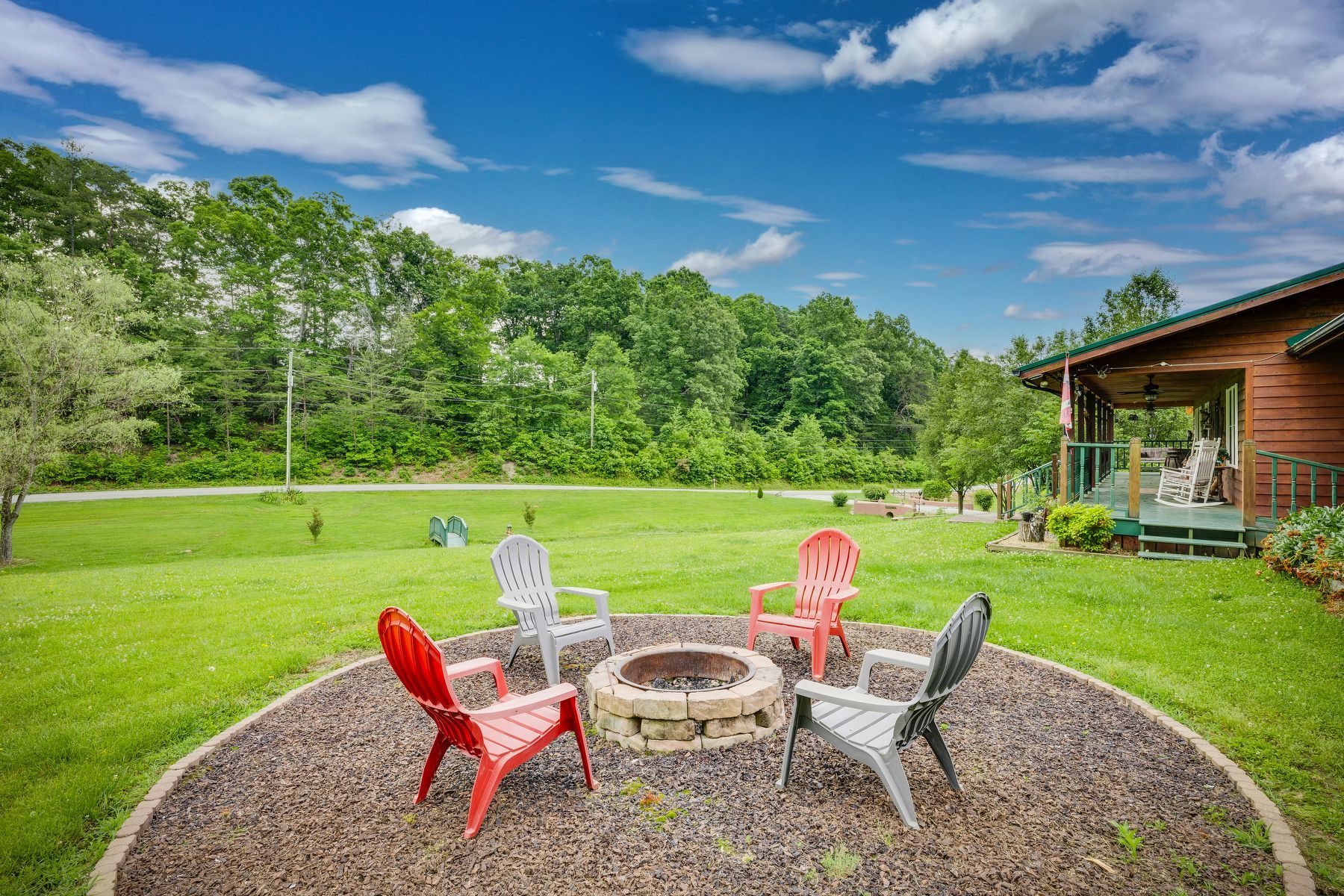 Fire pit in the middle of a lush green field with chairs around it.