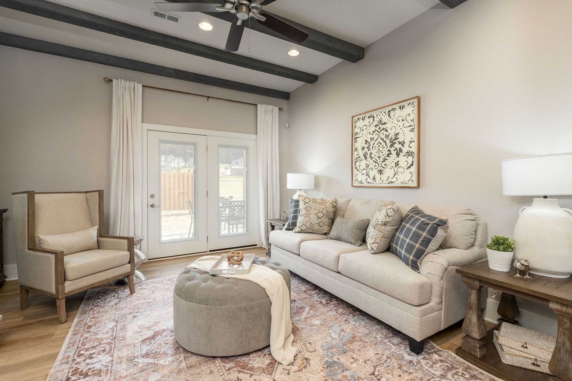 A living room with a couch , chair , ottoman and ceiling fan.