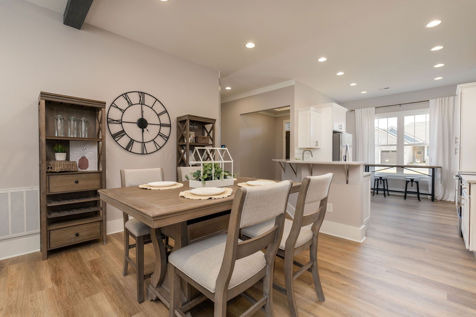 A dining room with a table and chairs and a clock on the wall.