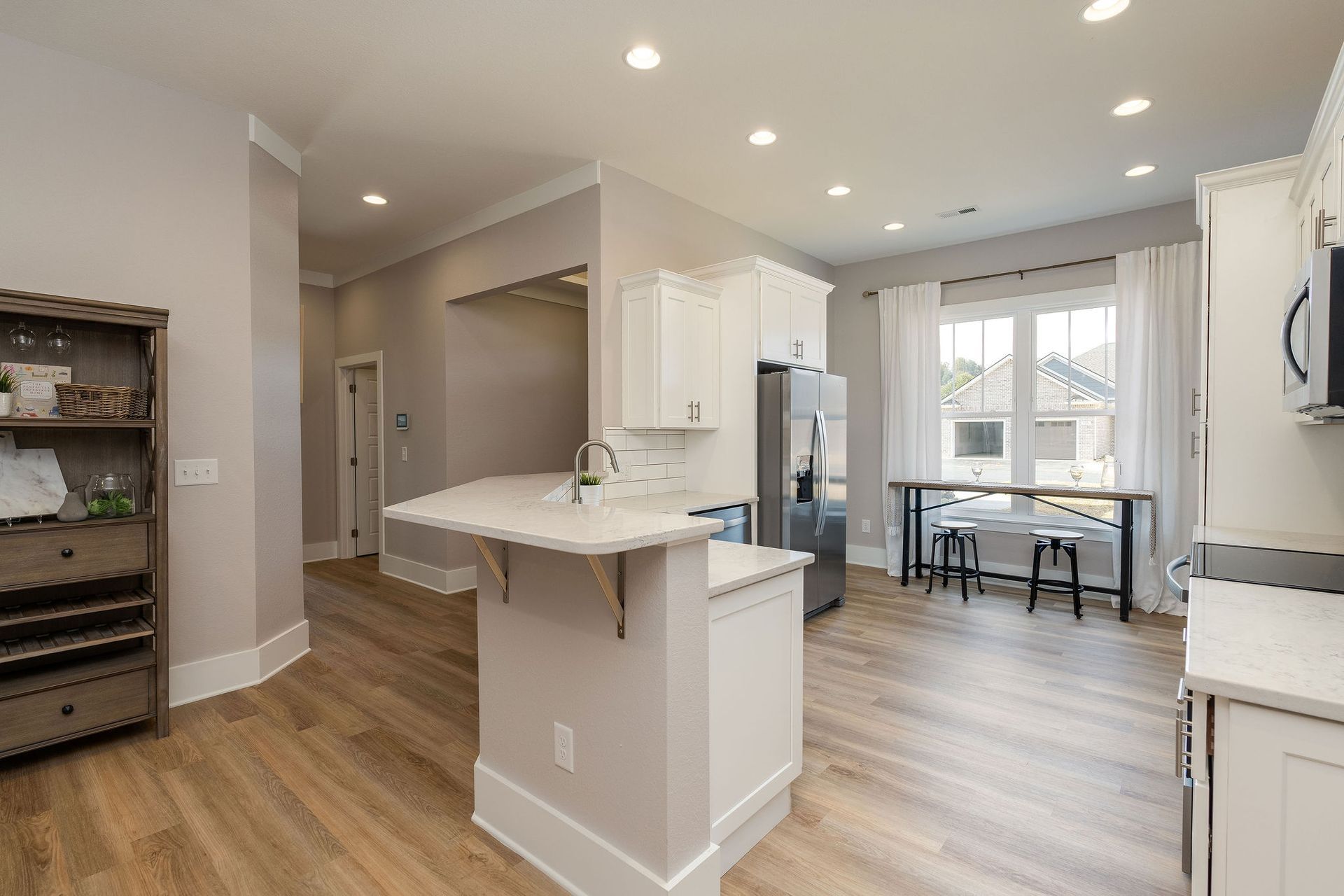 A kitchen with white cabinets and hardwood floors in a house.