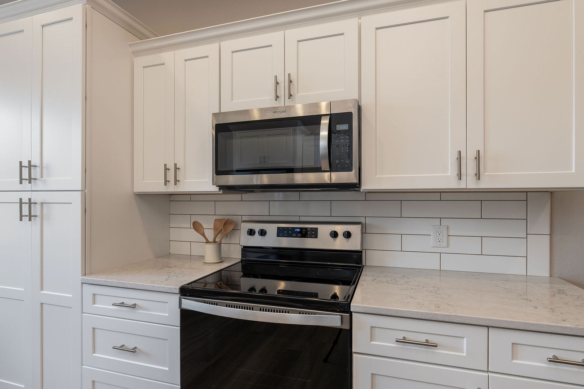 A kitchen with white cabinets , a stove and a microwave.