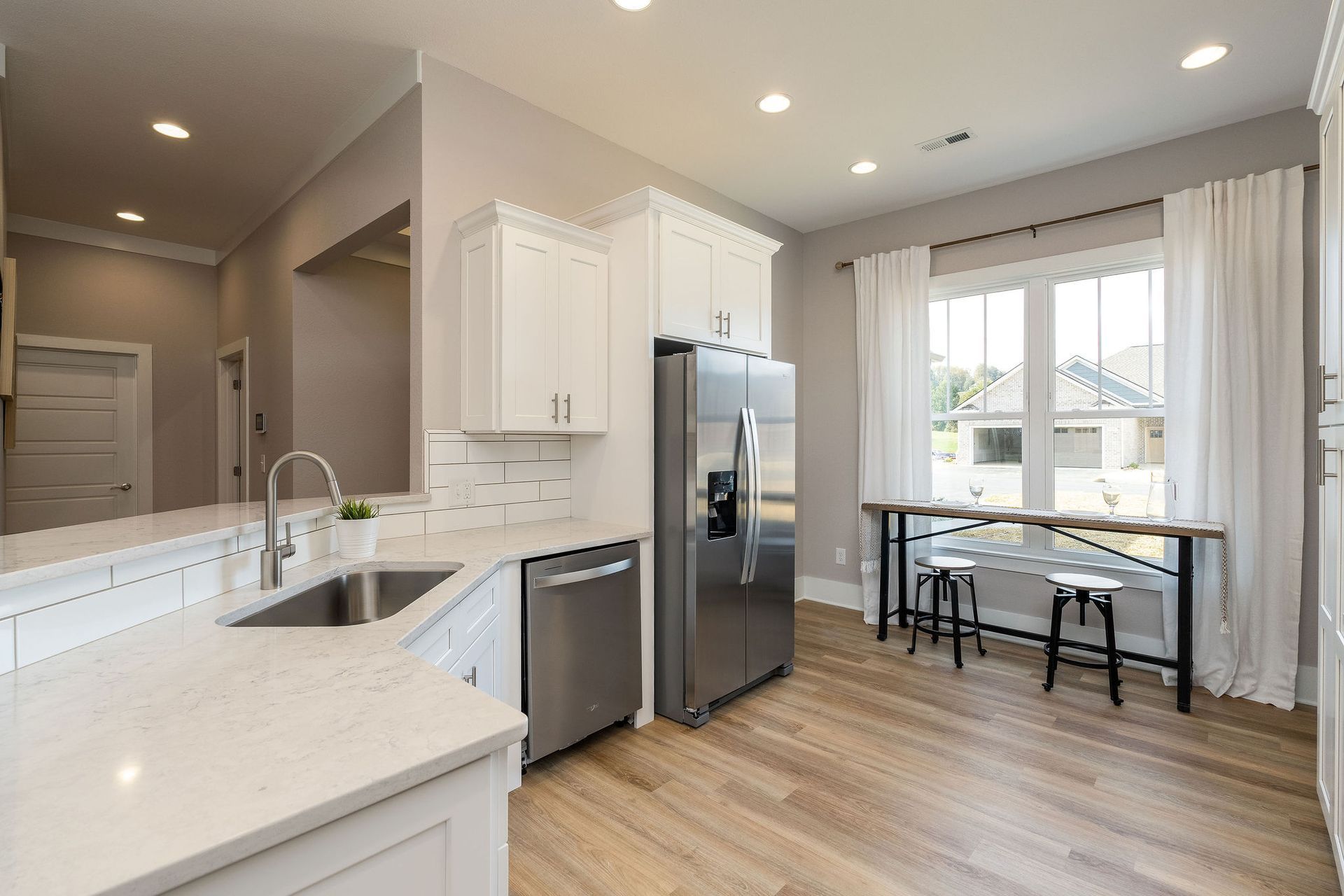 A kitchen with white cabinets , stainless steel appliances , a refrigerator and a sink.