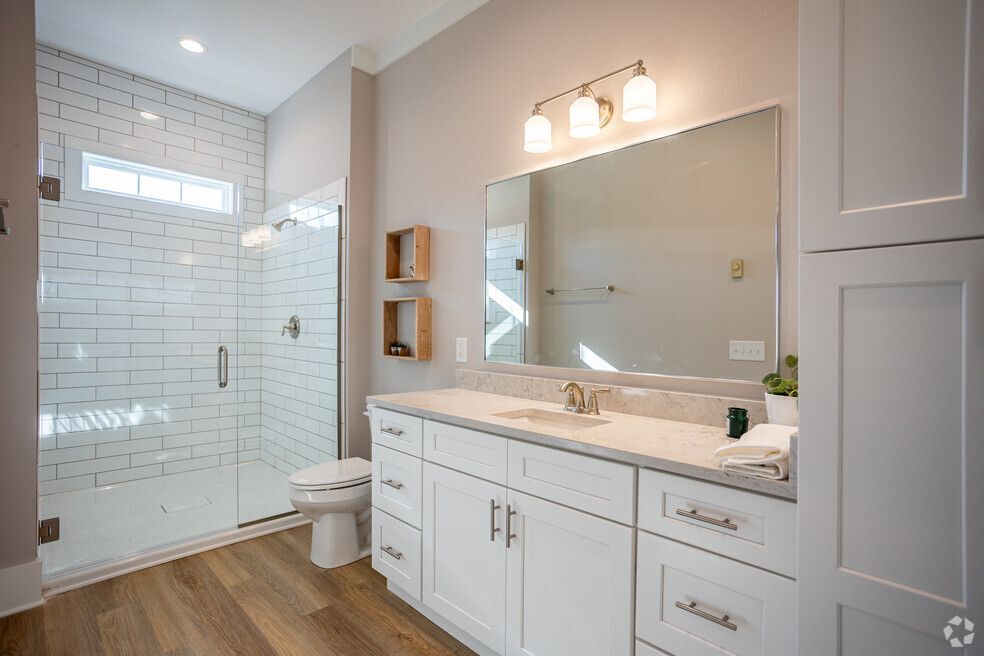 A bathroom with a toilet , sink , mirror and walk in shower.