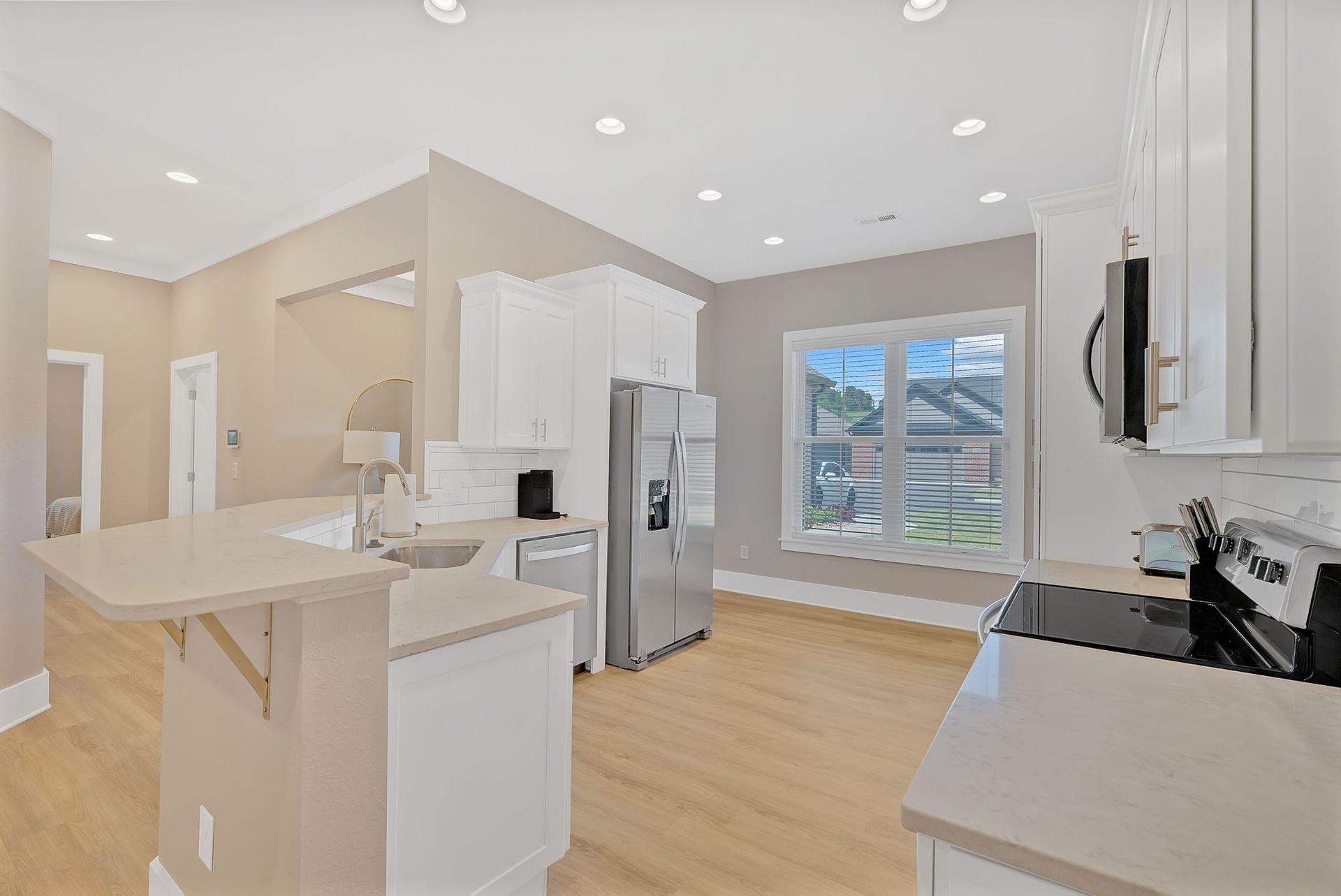 A kitchen with white cabinets , stainless steel appliances , hardwood floors and a refrigerator.