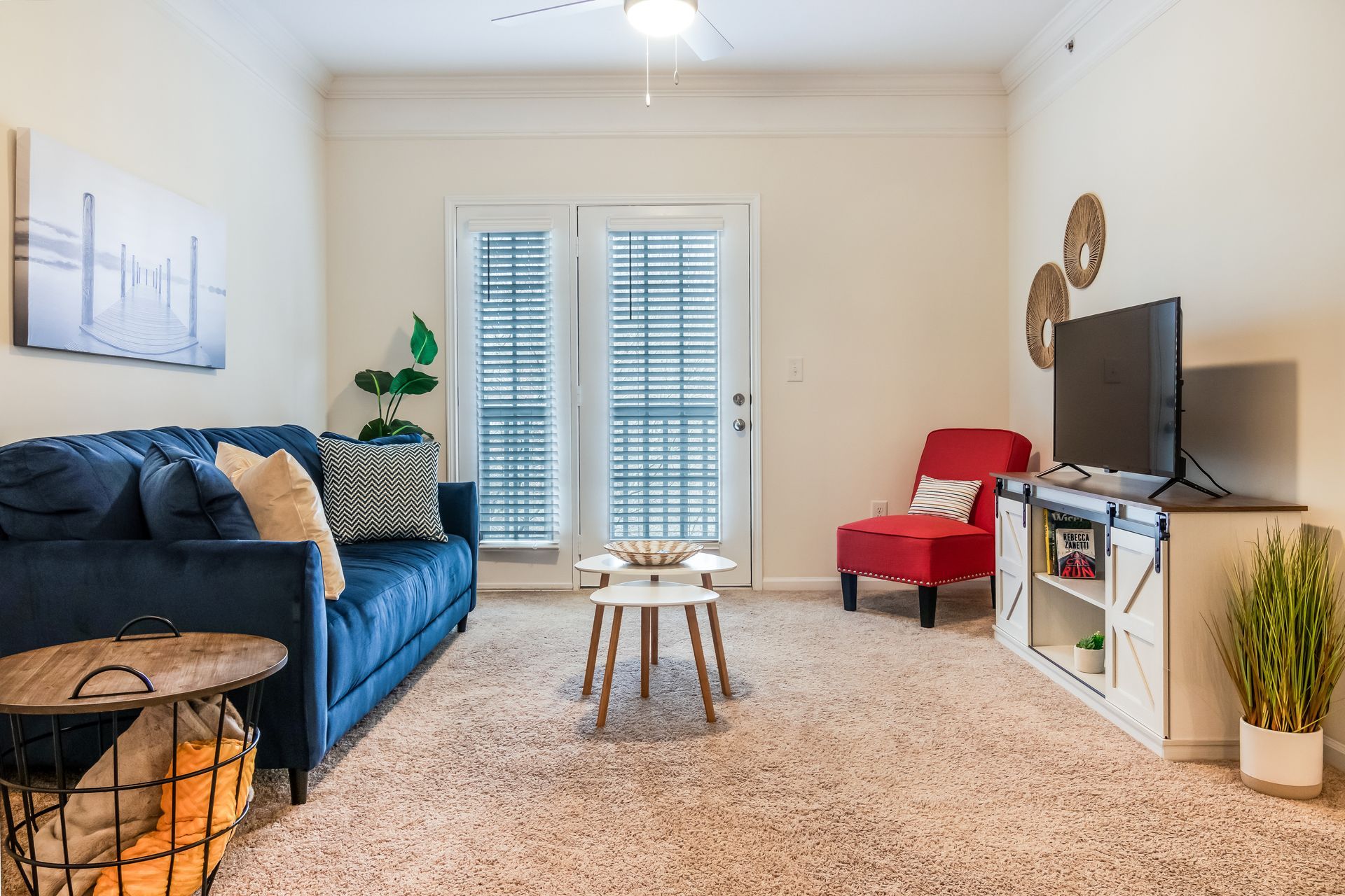 Modern furnished living room in Johnson City with a blue couch , a red chair , a television and a ceiling fan.