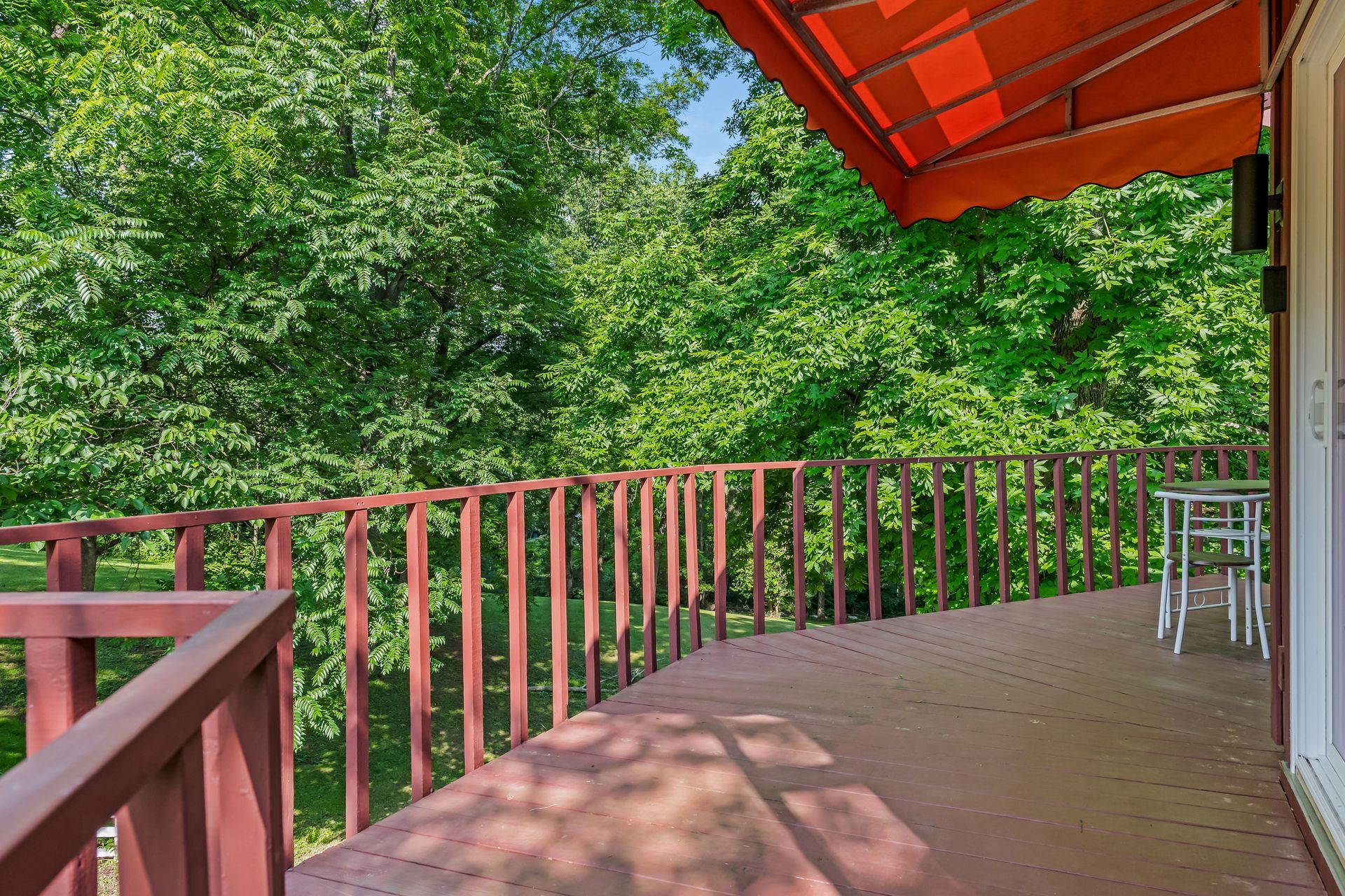 A large deck with a red railing and an orange awning surrounded by trees.