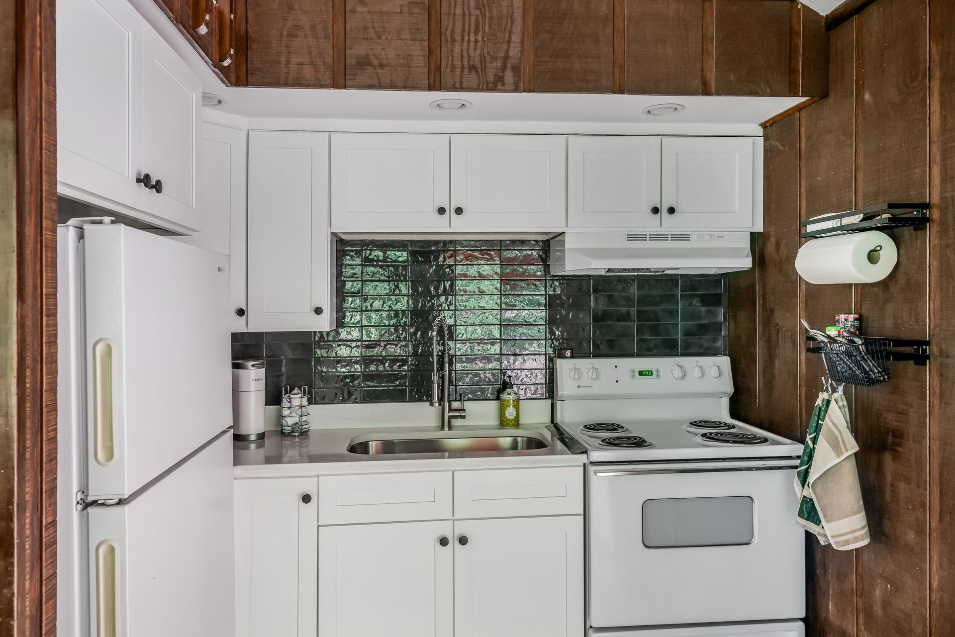 A small kitchen with white cabinets , a stove , a refrigerator , and a sink.