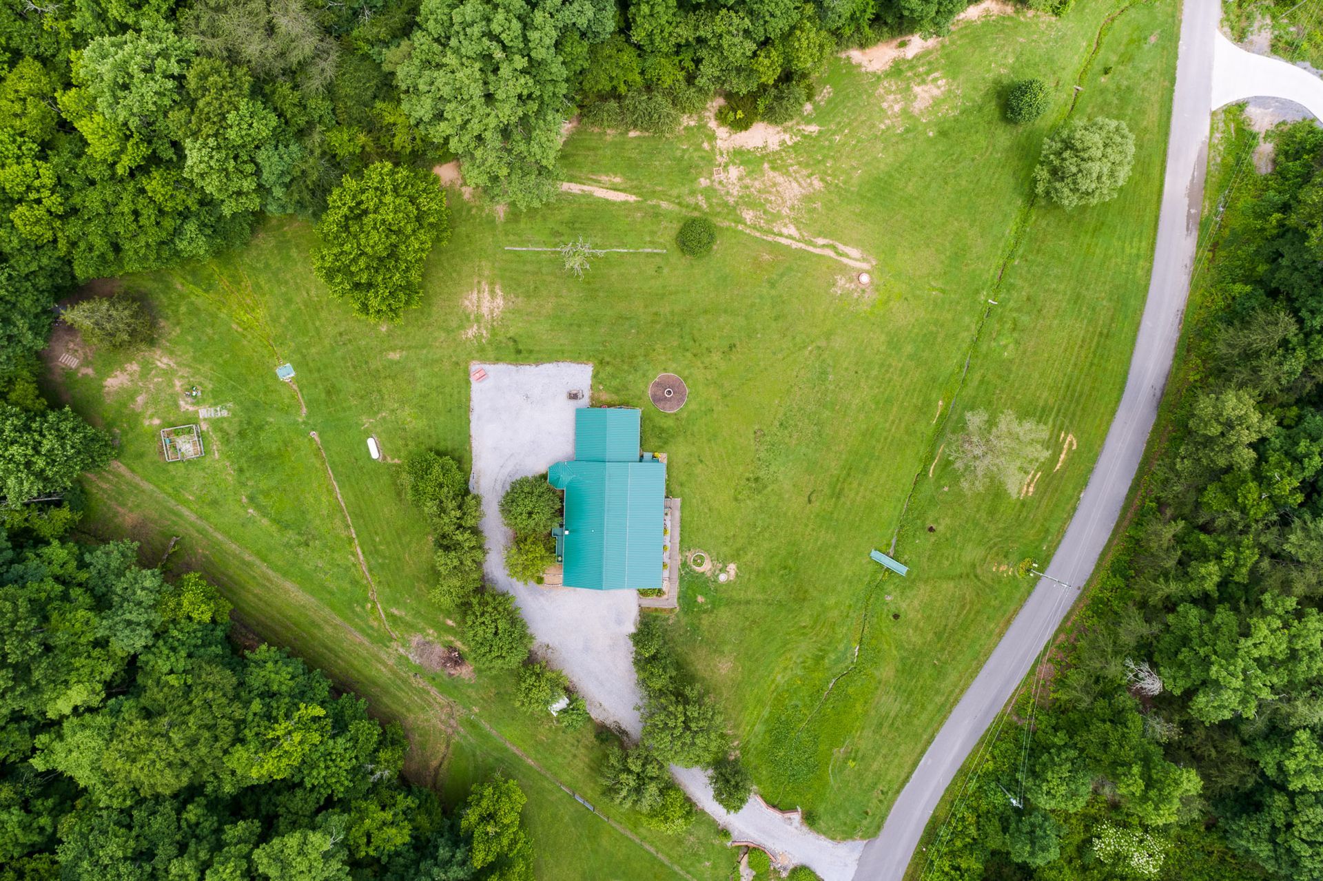 An aerial view of a house in the middle of a lush green field surrounded by trees.