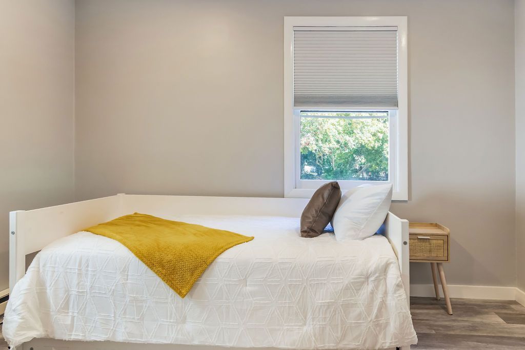 Bed with a yellow blanket on it is in a bedroom next to a window, Mystic, CT