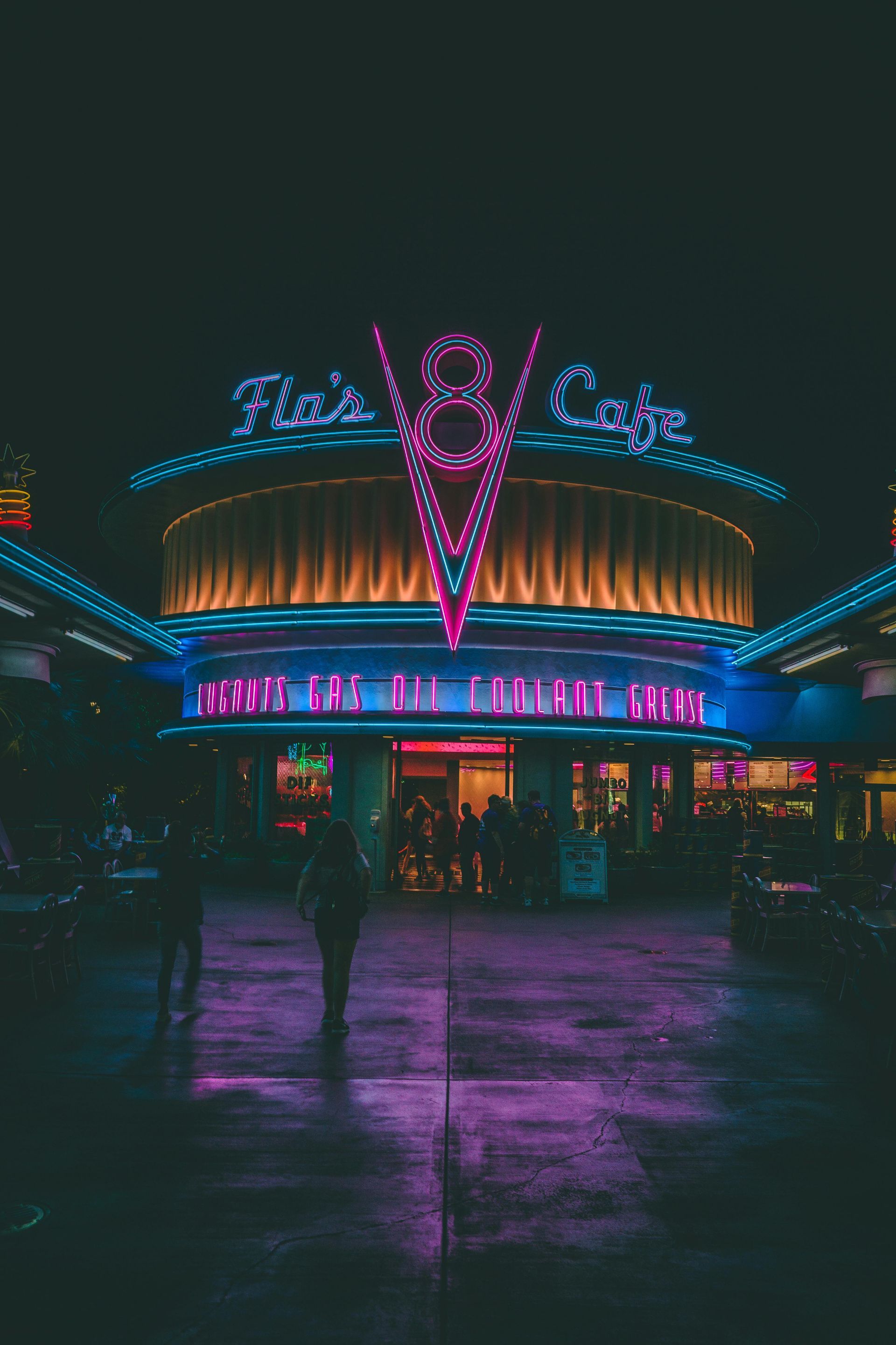 A person is walking in front of a neon lit building at night.
