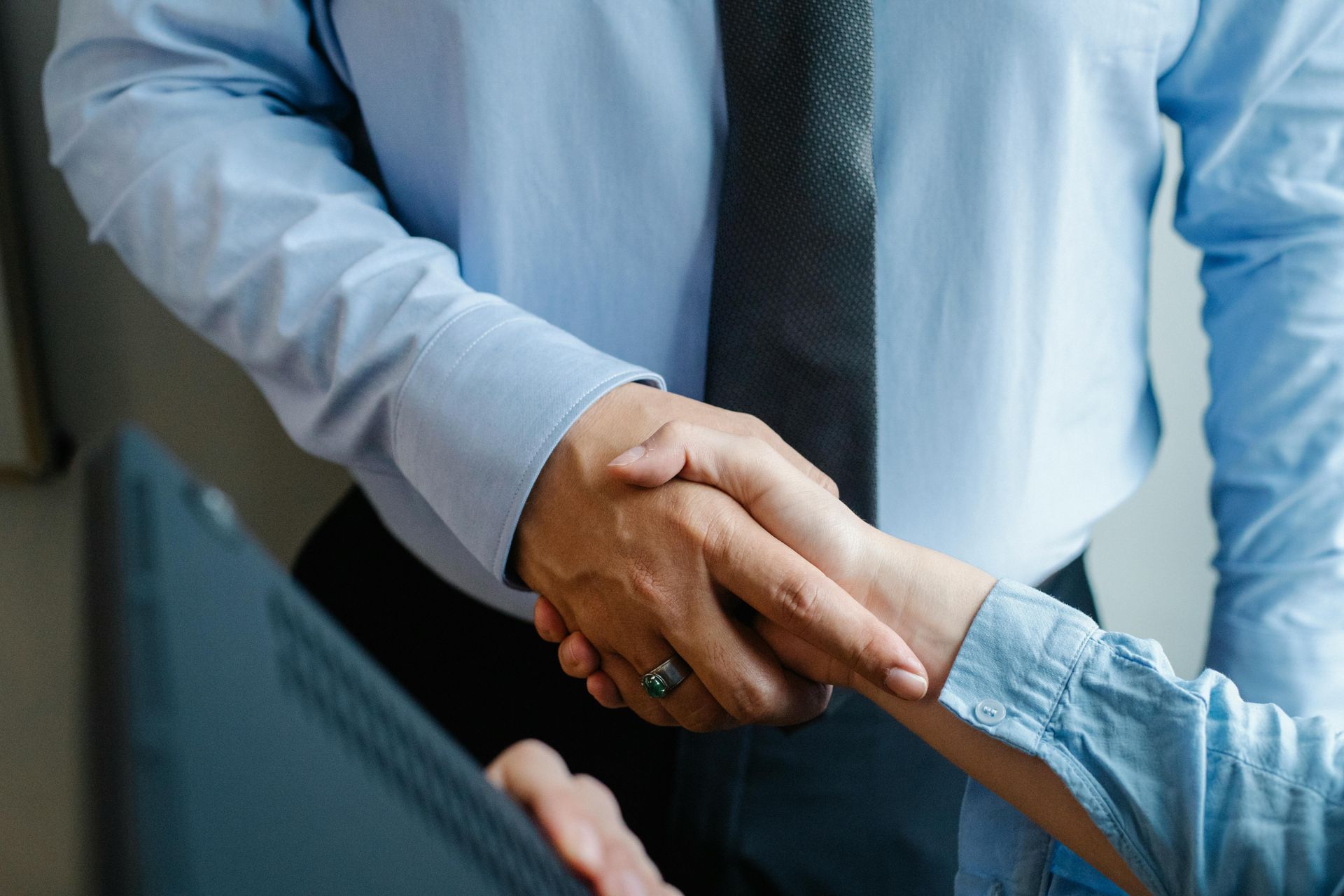 A man in a blue shirt and tie is shaking hands with a woman.