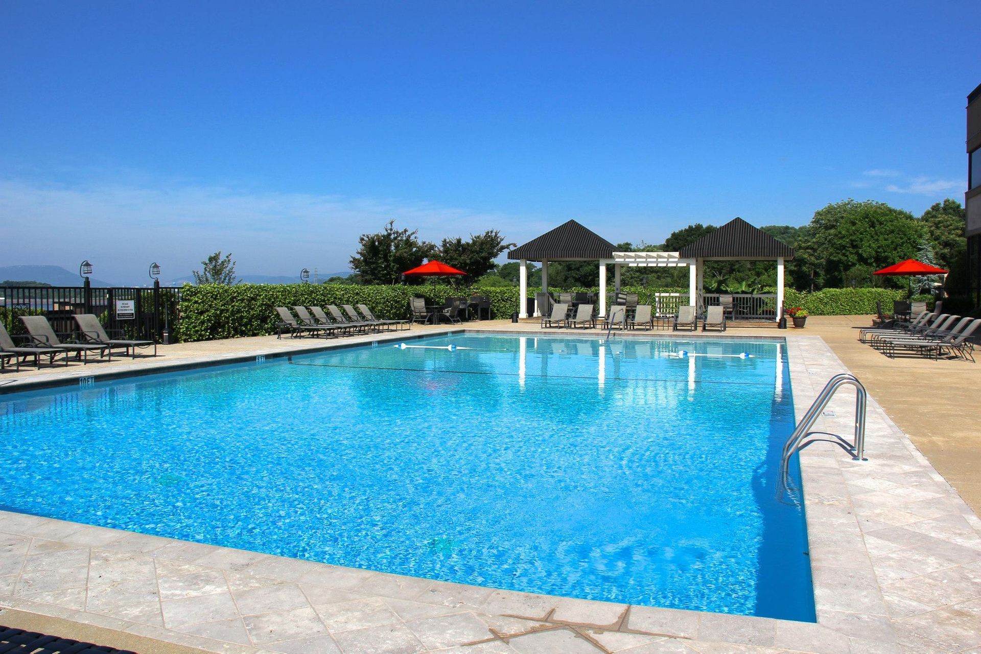 A large swimming pool surrounded by chairs and umbrellas on a sunny day.