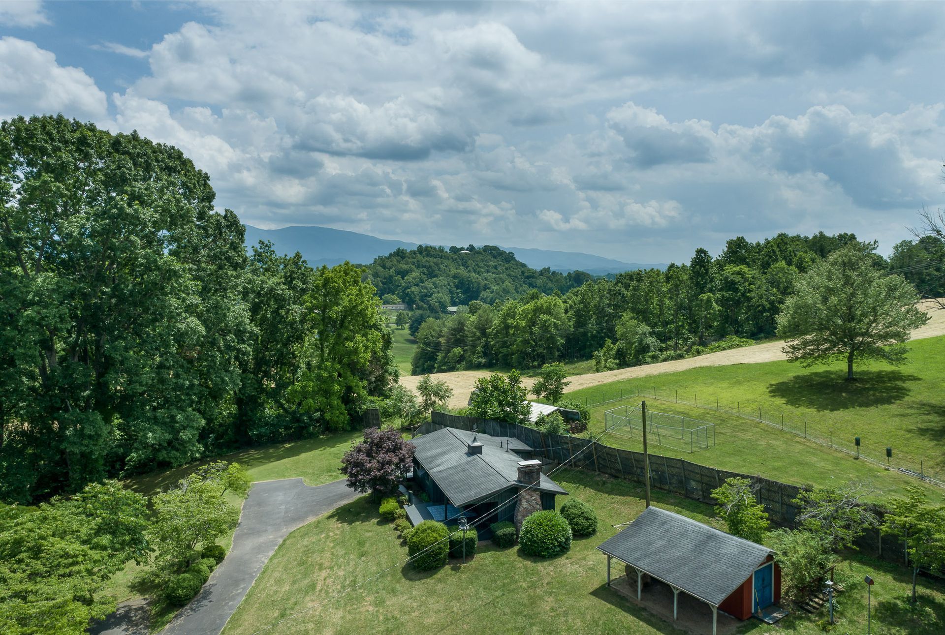 An aerial view of a house in the middle of a field with mountains in the background.