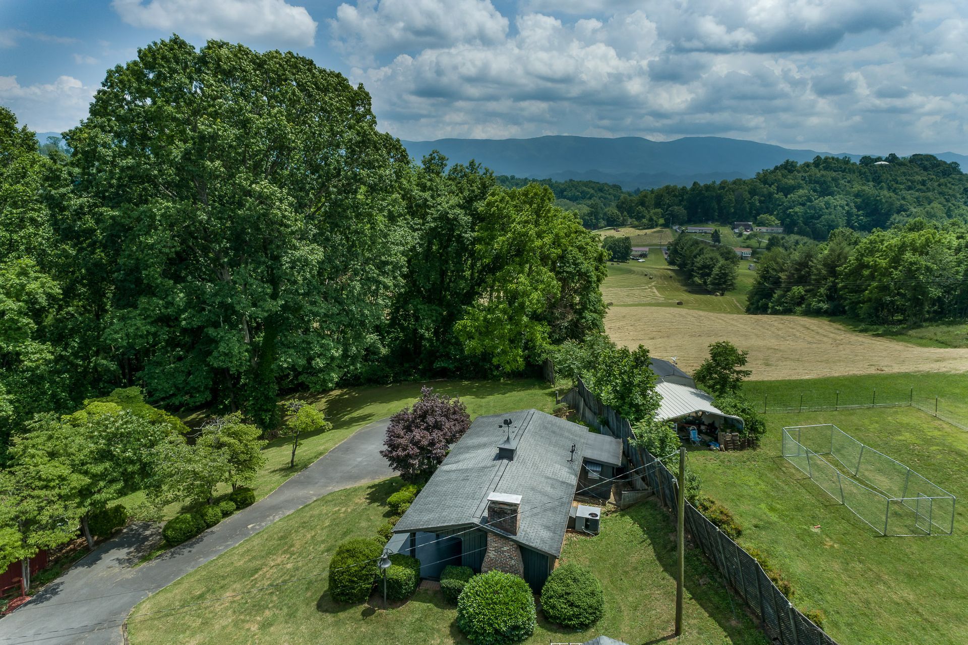 An aerial view of a house in the middle of a field with mountains in the background.