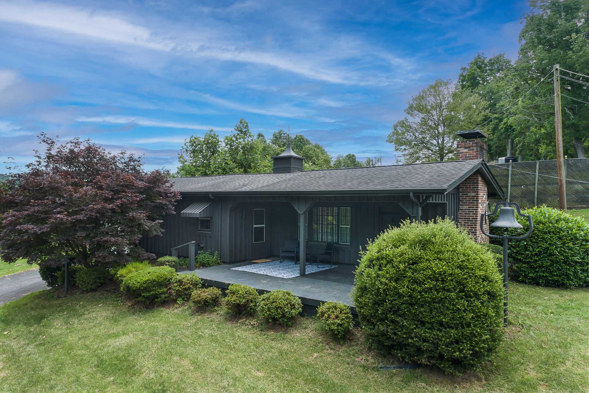 A small black house with a porch in the middle of a lush green field.