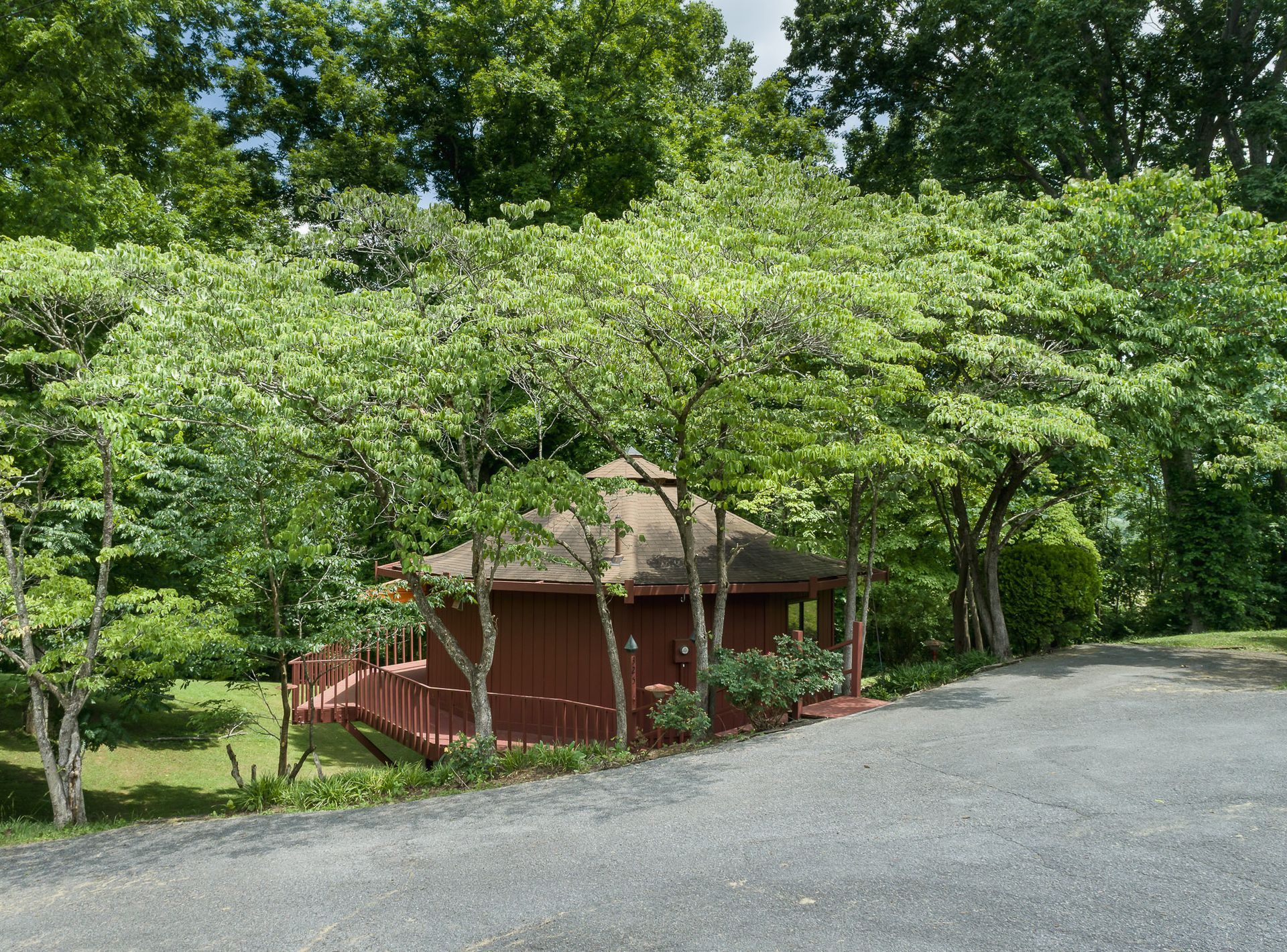 A red house with a deck is surrounded by trees
