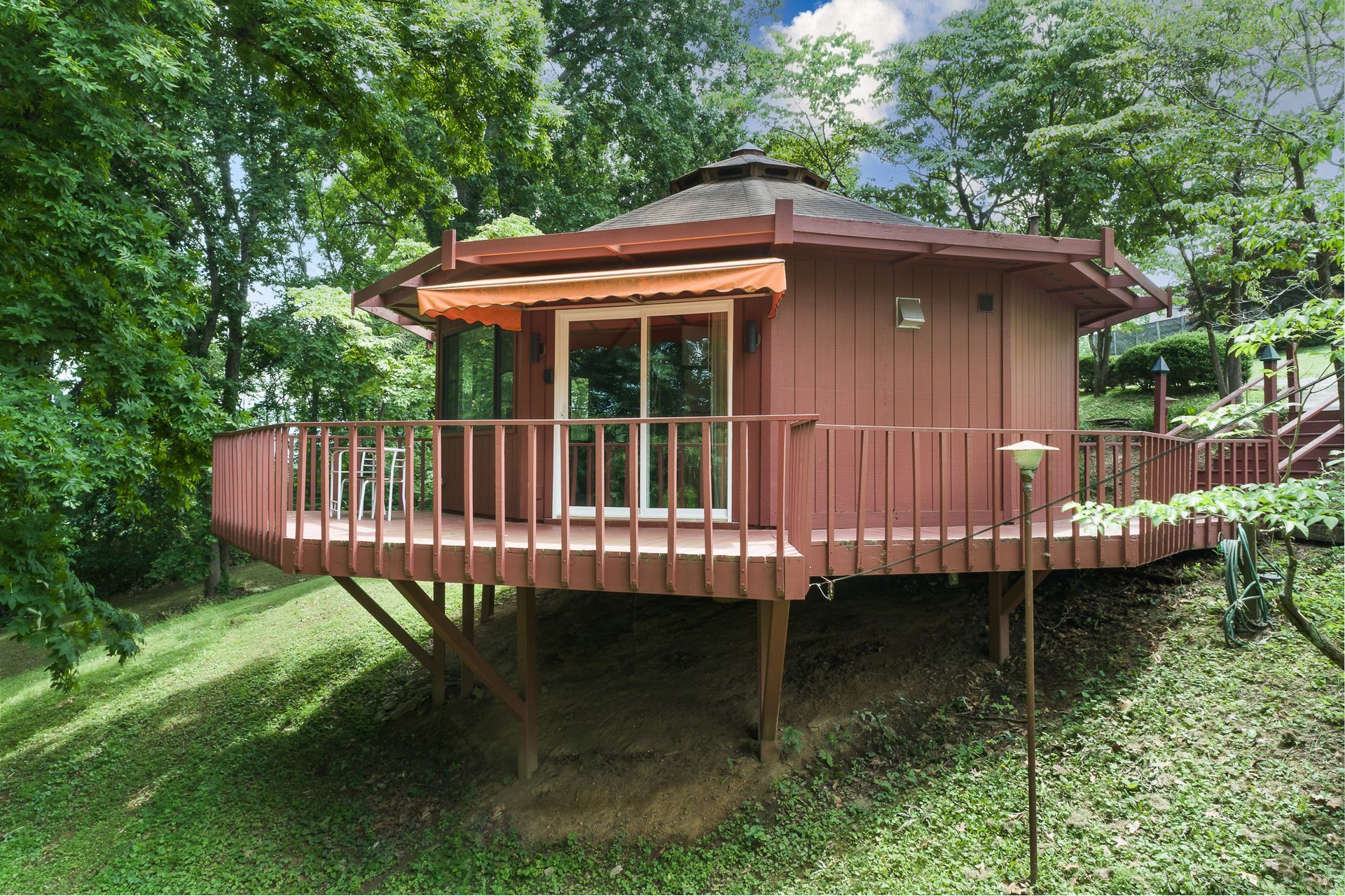 A small house with a large deck is surrounded by trees.