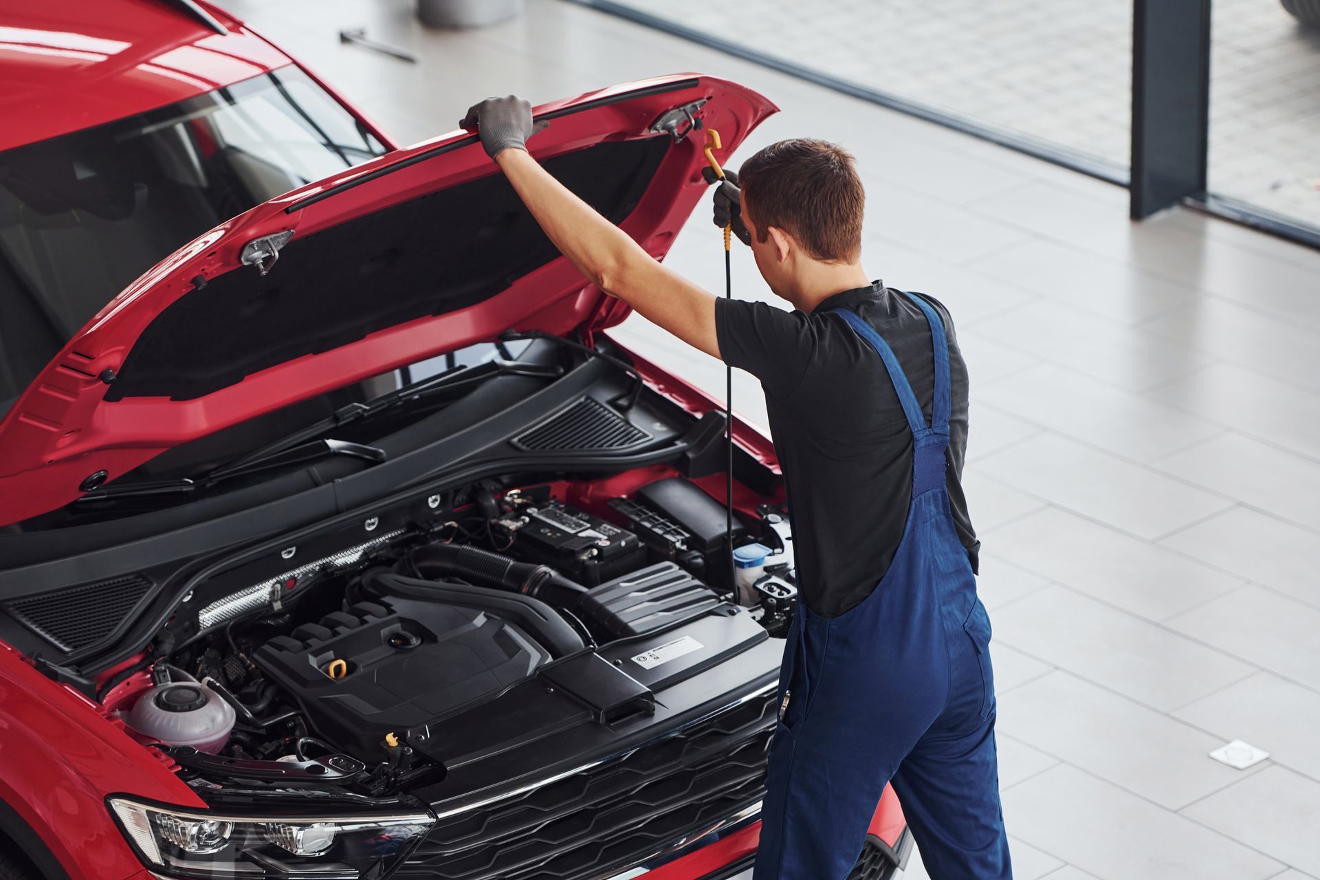 Top view of male worker in uniform that repairs red automobile.