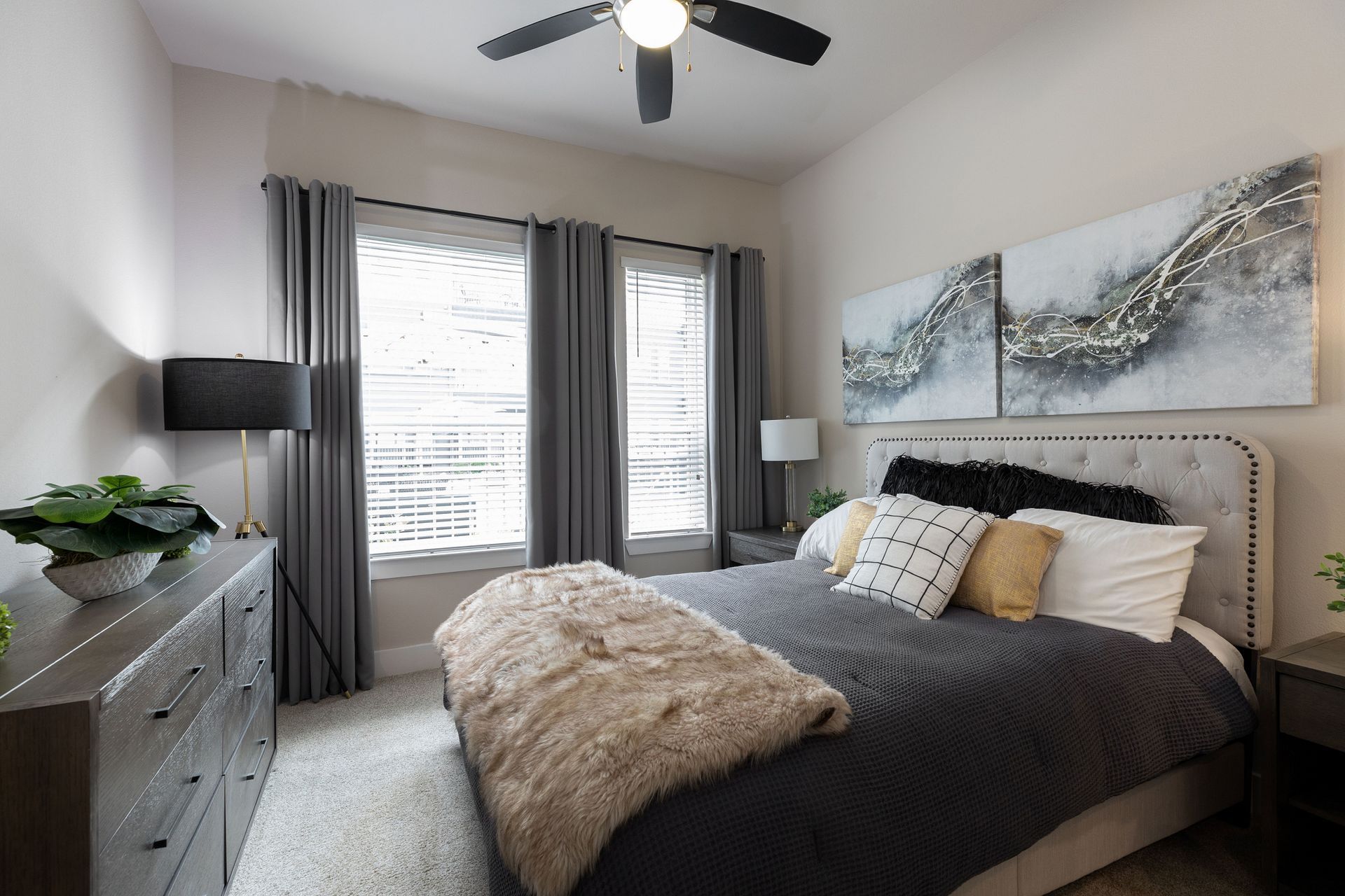 A bedroom with a bed , dresser , lamp and ceiling fan.