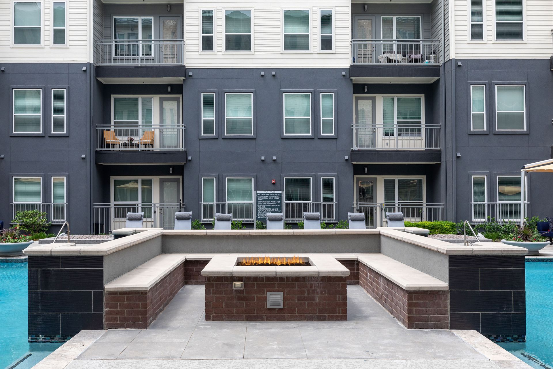 A fire pit in front of a building next to a pool.