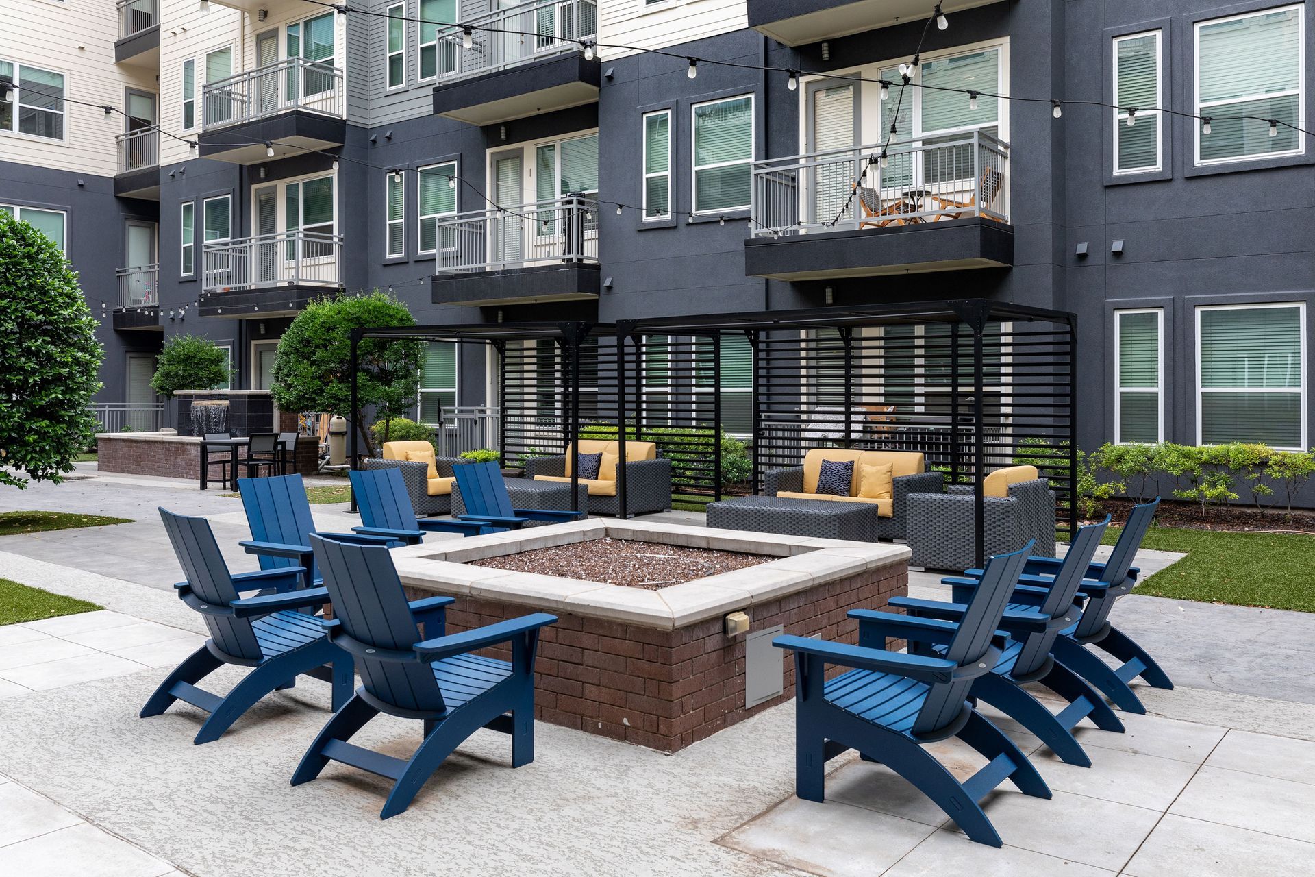A fire pit is surrounded by blue chairs in front of a building.