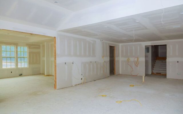 Room interior being painted; gray floor, two paint trays, brush, roller, ladder, masking tape.